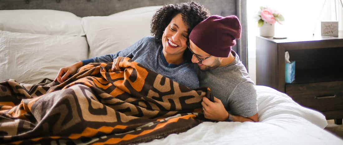 two people lying on a bed under a kuba cloth throw from the congo 